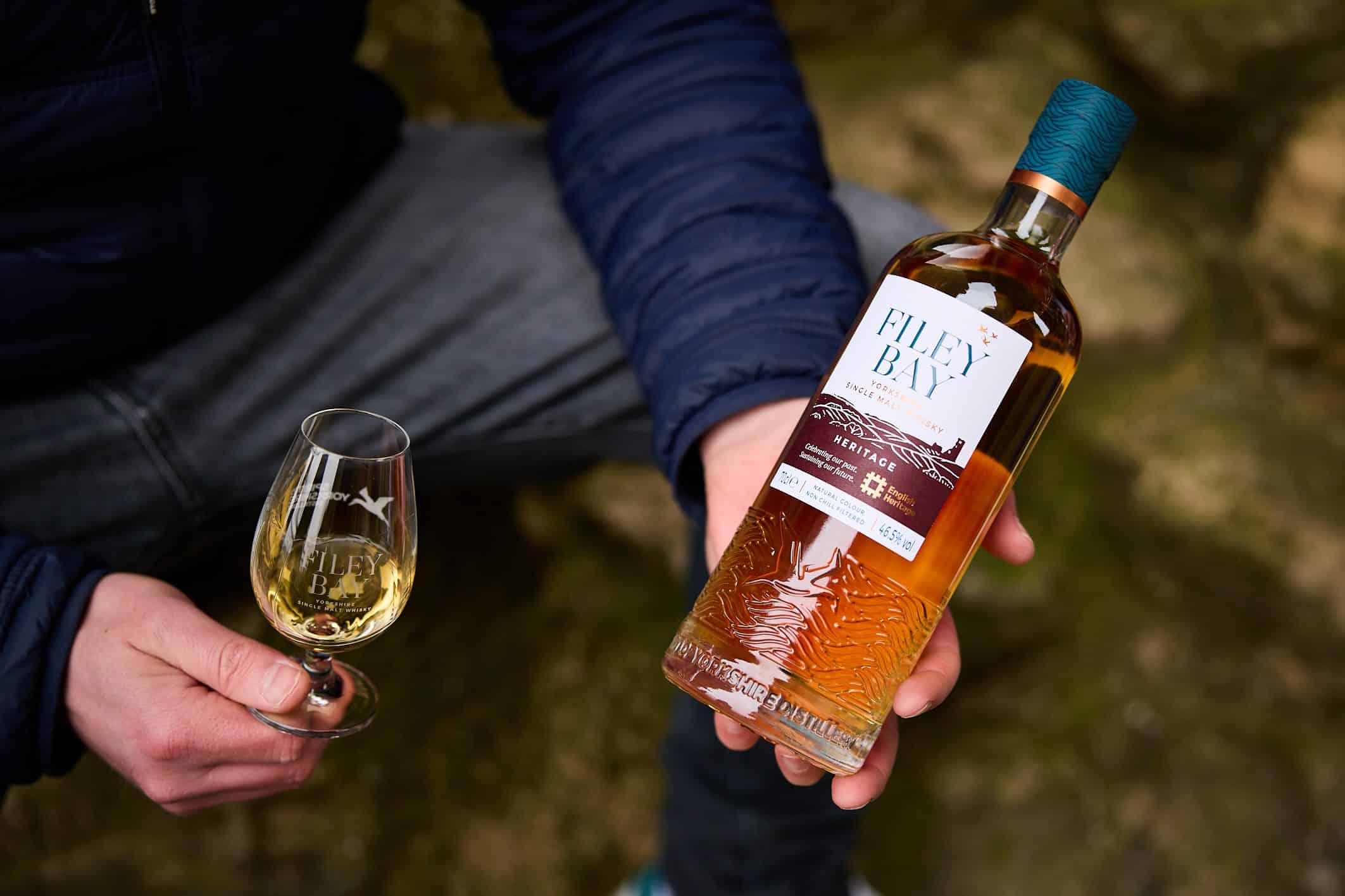 One hand holds a bottle of Filey Bay Heritage, with a glass in another